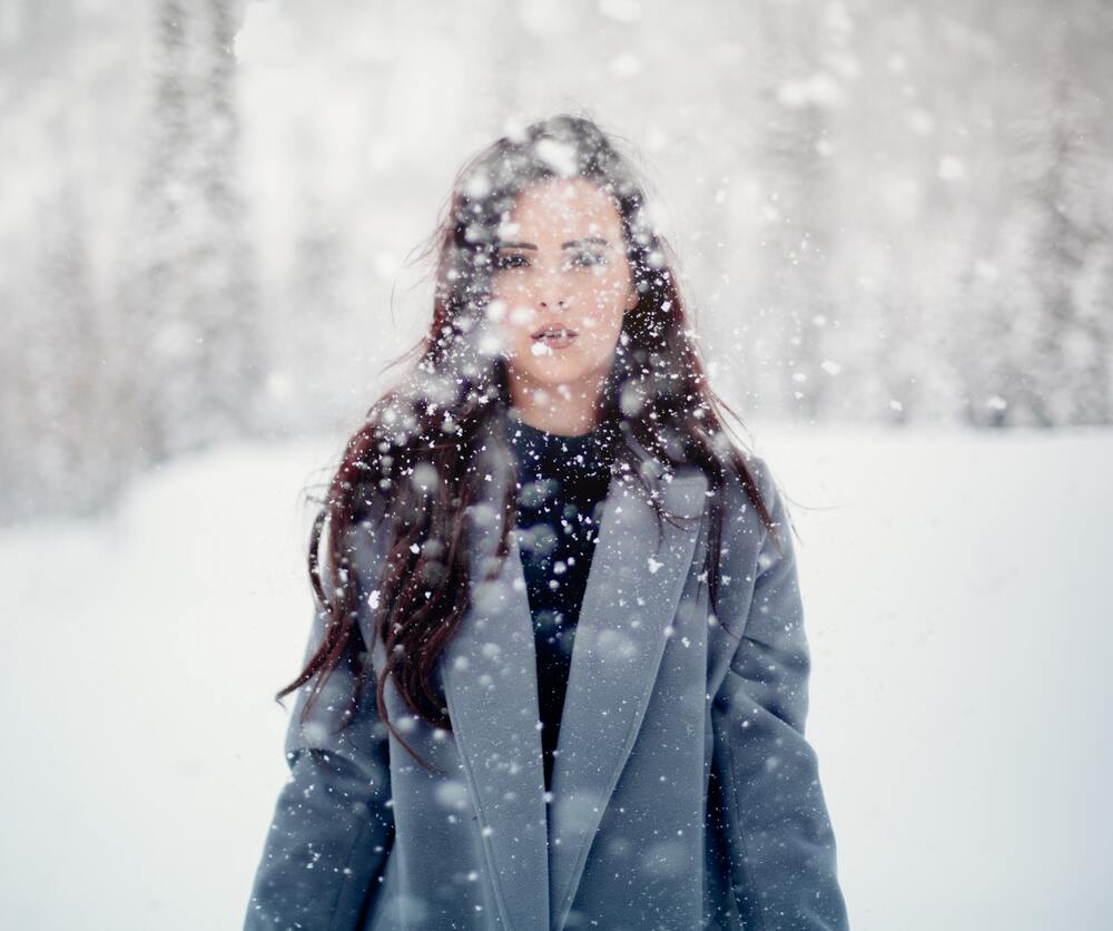 Devojka sa kaputom prekrivena sneznim pahuljama.