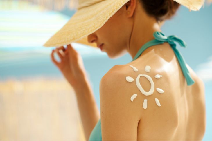 Žena sa šeširom se sunča i štiti se od opekotina od sunca kremom.